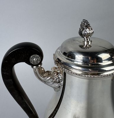 a silver coffee pot with a black handle on a table