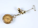 une montre de poche en or suspendue à une chaîne sur une surface blanche