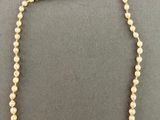 a white pearl necklace with a gold clasp on a black background