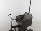 une petite poussette jouet noire avec des roues posée sur une surface blanche