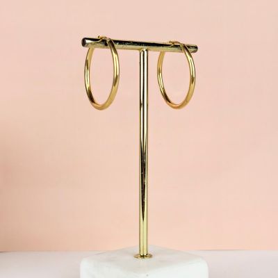 une paire de boucles d'oreilles créoles en or posée sur un socle en marbre
