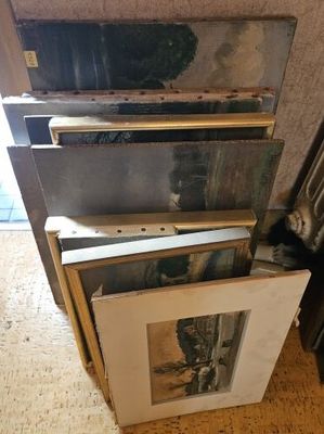 Plusieurs photos encadrées sont empilées les unes sur les autres par terre.
