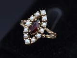 a close up of a gold ring with a red stone and pearls