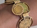 a gold bracelet with a coin on it on a woman ' s arm