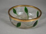 a glass bowl with a gold rim and green leaves on it