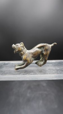 une statue en bronze représentant un chien courant sur une surface lisse