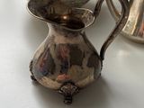 a silver pitcher sitting next to a silver pitcher on a table