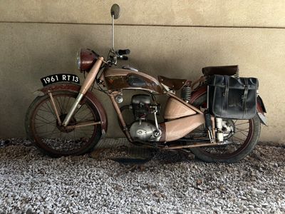 une vieille moto garée contre un mur, avec un sac posé dessus