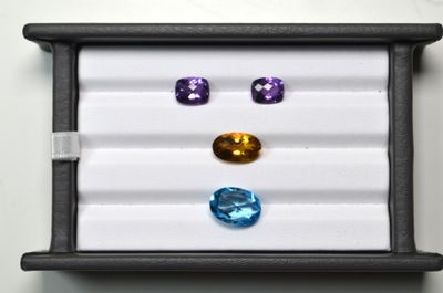 trois pierres précieuses de couleurs différentes dans une boîte noire posée sur une surface blanche