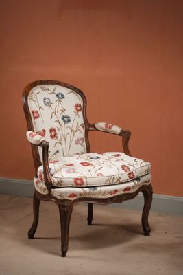 une chaise dont l'assise est recouverte d'un tissu à motifs floraux, placée devant un mur orange