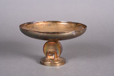 a silver bowl on a pedestal on a gray surface