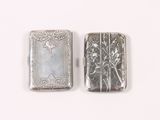two silver cigarette cases sitting next to each other on a white surface