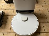 un robot blanc posé sur un sol carrelé, à côté d'un micro-ondes