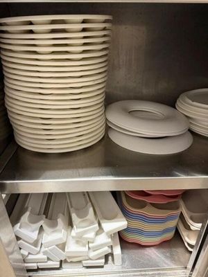 Plusieurs assiettes et bols sont empilés sur une étagère en métal dans une cuisine.