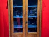 an old wooden cabinet with glass doors and a red wall