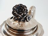 a silver teapot with a flower on top