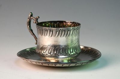 a silver cup and saucer sitting on a saucer