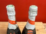 two bottles of brut on a wooden table with a red wall in the background