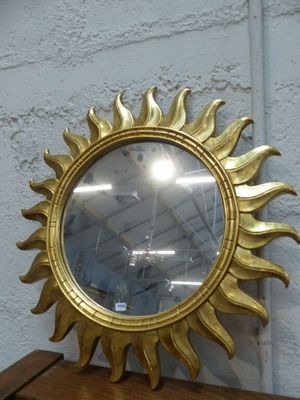 un miroir doré en forme de soleil posé sur une étagère en bois