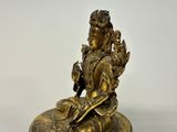 brass statue of a woman sitting on a rock with a bird in her hand