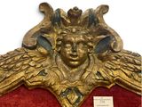 a gold sculpture of a winged head on a red chair