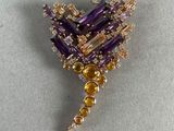 une image représentant une broche ornée de pierres violettes et jaunes