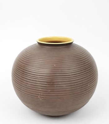 un vase marron bordé de jaune, posé sur une surface blanche