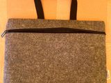 un sac d'ordinateur portable gris avec des fermetures éclair noires, posé sur une boîte en carton