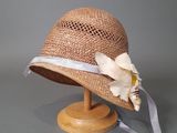 chapeau de paille beige orné d'un ruban blanc et d'une fleur, posé sur un support en bois