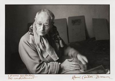 photographie en noir et blanc d'une vieille femme assise à une table