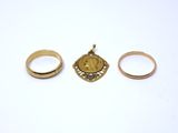 two gold rings and a gold pendant on a white surface