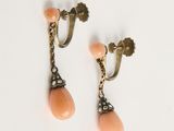 une photo représentant une paire de boucles d'oreilles couleur pêche posées sur une surface blanche