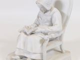 une statue représentant une femme assise sur une chaise en train de lire un livre