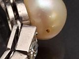 a white pearl and a silver bracelet on a black surface