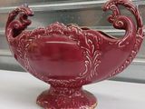 a red vase with a bird on it sitting on a window sill