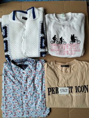 trois t-shirts et un pull sont posés sur une boîte en carton