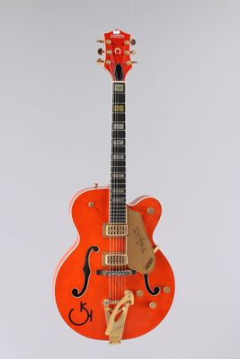 une guitare électrique orange suspendue à une ficelle sur un mur blanc