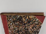 an old book with a red cover sitting on top of a white table