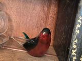 a glass bird sitting on a book shelf next to a wine glass