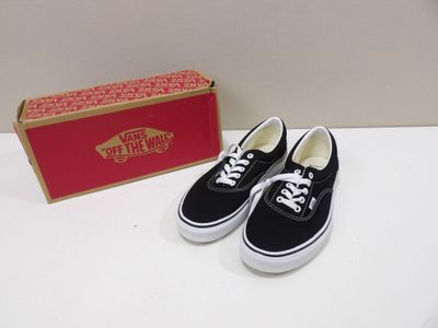 une paire de baskets sans lacets noires et blanches à côté d'une boîte rouge