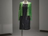 une robe noire ornée de paillettes vertes, posée sur un présentoir pour mannequin