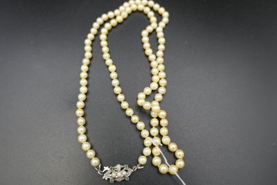un collier de perles blanches muni d'un fermoir en argent, posé sur un fond noir
