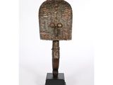 une statue en bronze représentant un homme à la tête disproportionnée, posée sur un socle en bois