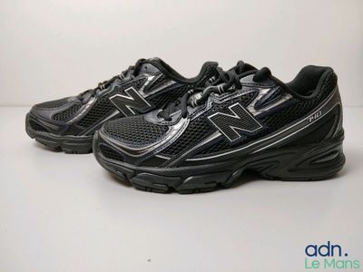 La chaussure de course New Balance 990 est noire et comporte une bande argentée.