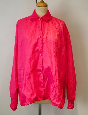 une chemise rose posée sur un mannequin, devant un mur blanc