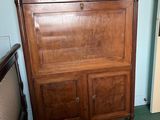 a wooden cabinet in the corner of a room with a painting on the wall