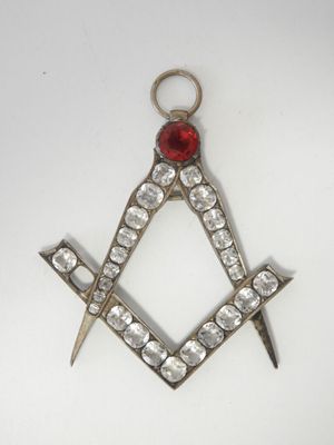 une image représentant un pendentif maçonnique en forme d'équerre et de compas, orné d'une pierre rouge