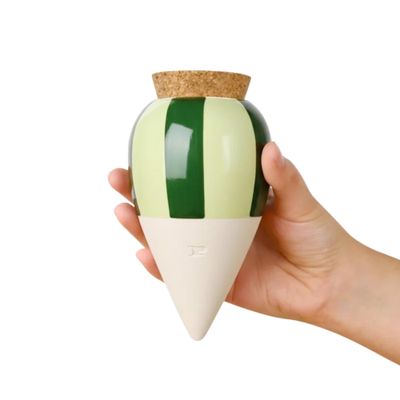 a hand holding a green and white vase with a cork top