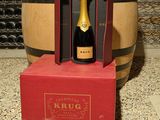 une bouteille de vin dans un coffret rouge devant un tonneau de vin