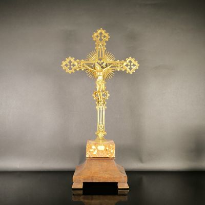 un crucifix en or posé sur un socle en bois, sur fond gris